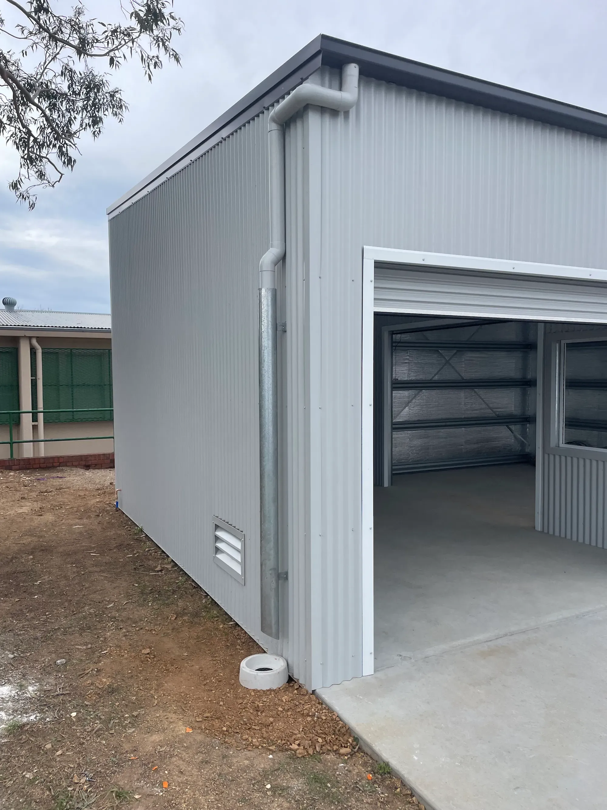New grey PVC downpipe and galvanised stormwater riser run down the corner of a Colorbond shed to a slab inspection point
