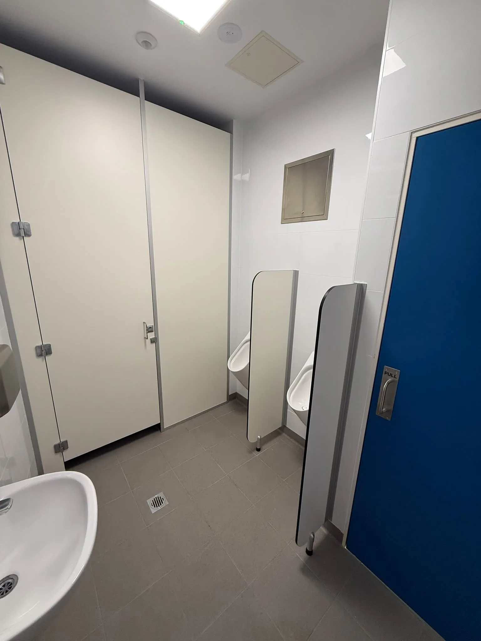 Refurbished commercial washroom with toilet cubicles, wall-hung urinals behind privacy screens and a vitreous china hand basin